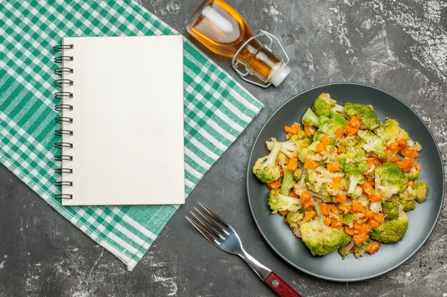 Ensalada de verduras frescas y saludables, toalla verde despojada con botella de aceite caído y cuaderno