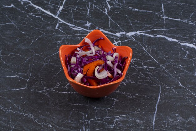 Ensalada de verduras frescas en un tazón de naranja sobre piedra negra.