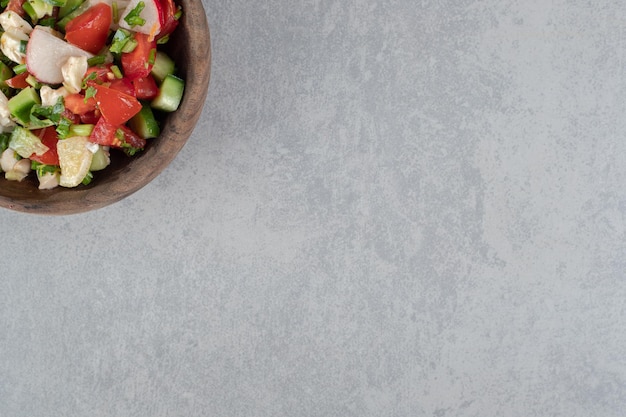 Ensalada de verduras con ingredientes mixtos en una taza de madera.