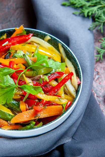 Ensalada de verduras de la mitad superior vista en un tazón chal azul ultramar en la mesa de color rojo oscuro