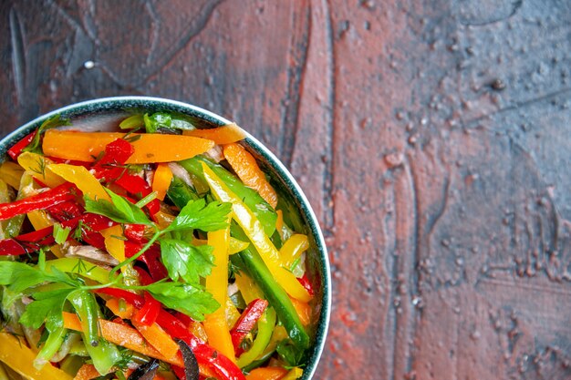 Ensalada de verduras de la mitad superior vista en un tazón en la mesa de color rojo oscuro con lugar de copia