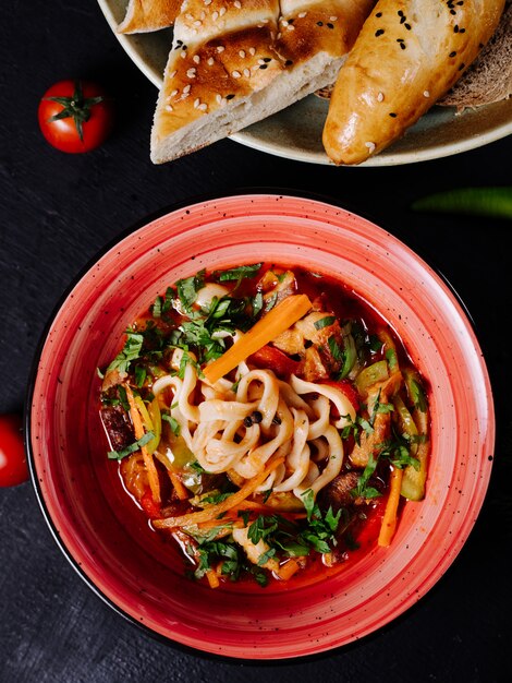 Ensalada de verduras mixtas en un recipiente rojo con pan.