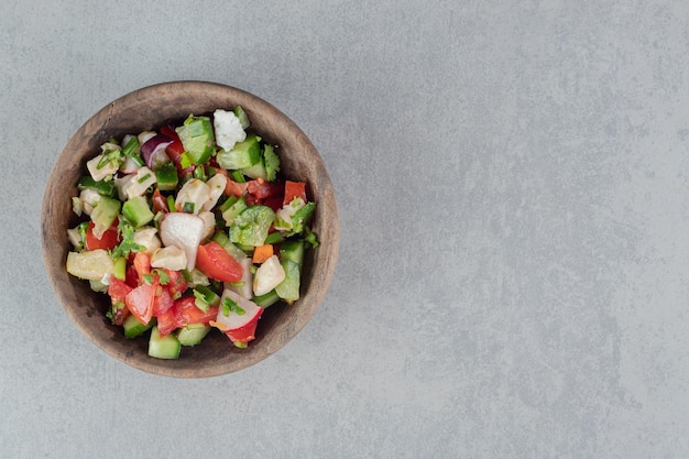 Ensalada de verduras mixtas en una taza de madera sobre la mesa de hormigón.