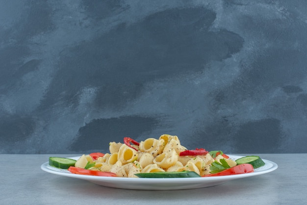 Ensalada de verduras en un plato blanco con deliciosos macarrones sobre fondo de mármol