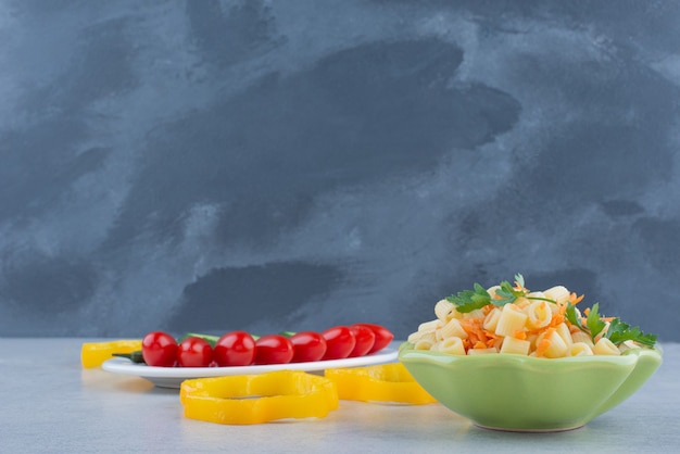 Ensalada de verduras en un plato blanco con macarrones en la superficie de mármol