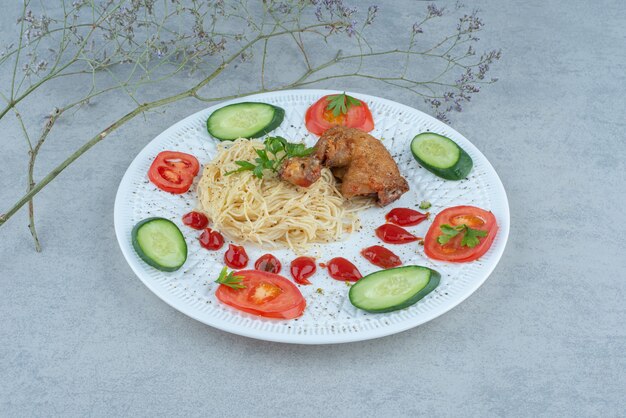 Ensalada de verduras en un plato blanco con pasta y pollo sobre fondo de mármol