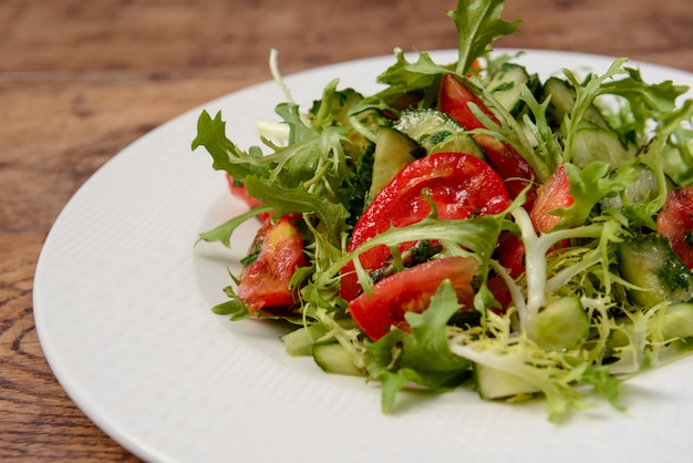 Ensalada de verduras en plato redondo blanco sobre mesa de madera.