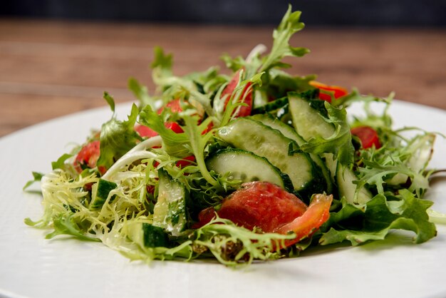 Ensalada de verduras en plato redondo blanco sobre mesa de madera.