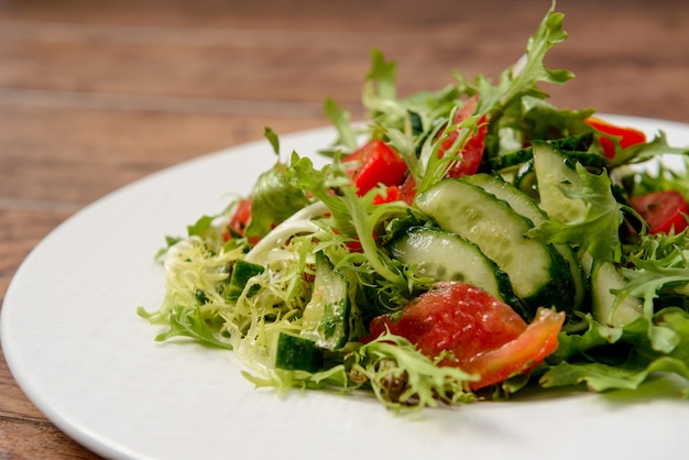 Ensalada de verduras en plato redondo blanco sobre mesa de madera.