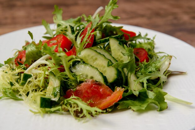 Ensalada de verduras en plato redondo blanco sobre mesa de madera.