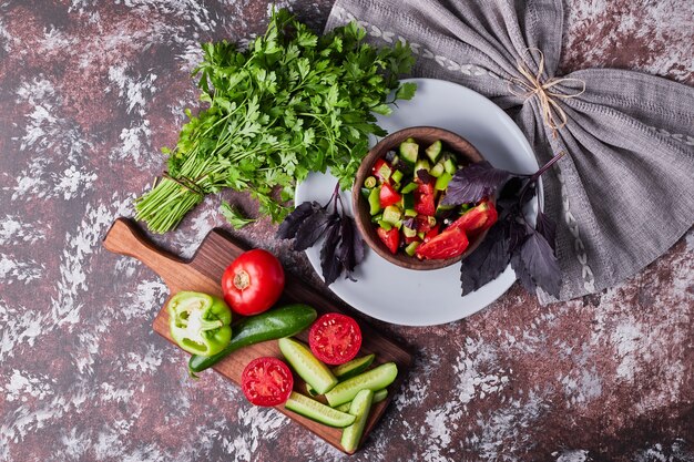 Ensalada de verduras en una taza de madera servida con hierbas sobre el mármol.