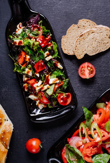 Ensalada de verduras con tomates dentro de una fuente de botella negra.