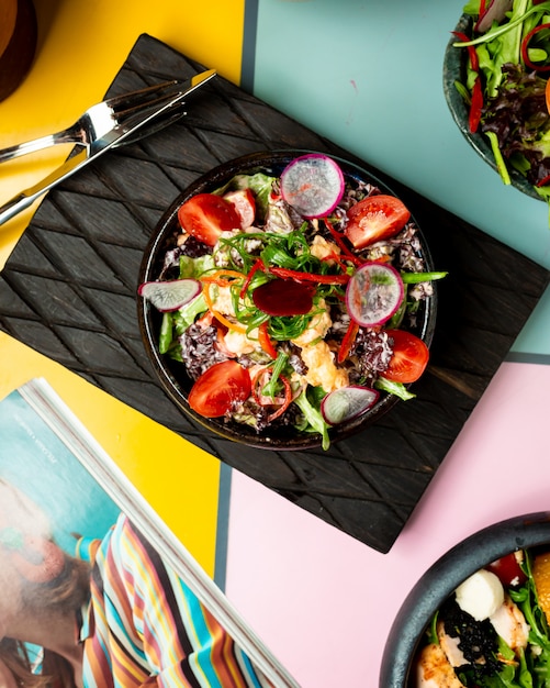 Ensalada de verduras con tomates en un tablero negro.