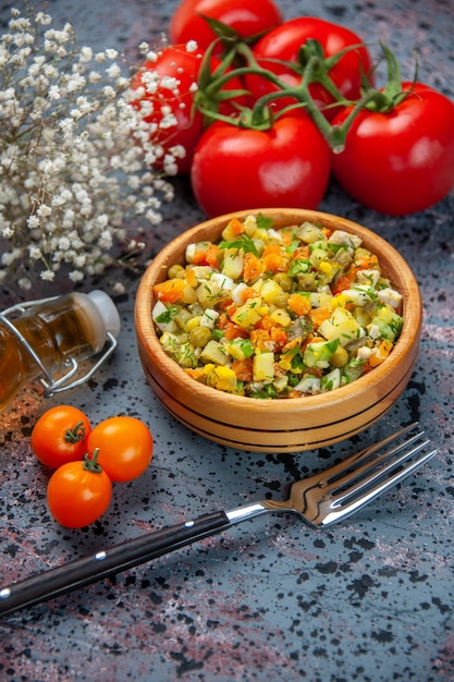 Ensalada de verduras vista frontal con tenedor y tomates sobre fondo azul claro