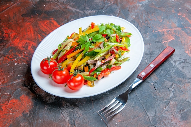 Ensalada de verduras de vista inferior en horquilla de placa ovalada sobre superficie oscura