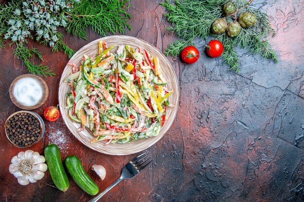 Ensalada de verduras de vista superior en plato tenedor tomates ramas de pino pepinos ajo en lugar libre de mesa rojo oscuro