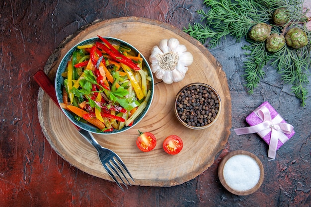 Ensalada de verduras de vista superior en un tazón tenedor ajo pimienta negra en rama de abeto de tablero rústico en mesa rojo oscuro