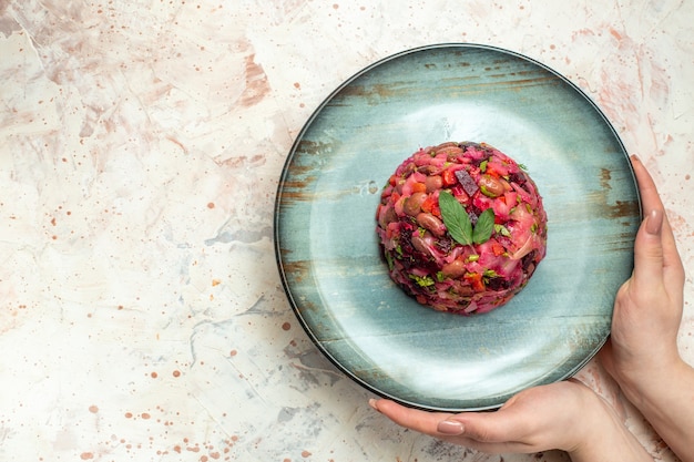 Ensalada de vinagreta de vista superior en plato ovalado en mano femenina en espacio libre de mesa gris claro