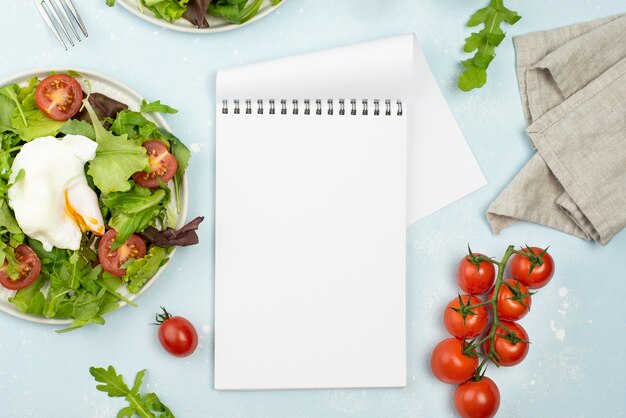 Ensalada de vista superior con huevo frito y tomates con bloc de notas en blanco