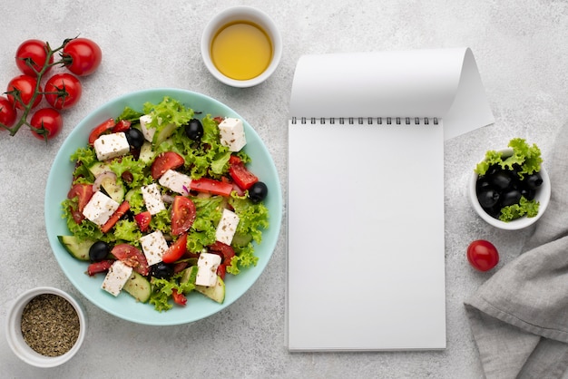 Ensalada de vista superior con queso feta, tomates y aceitunas con bloc de notas en blanco