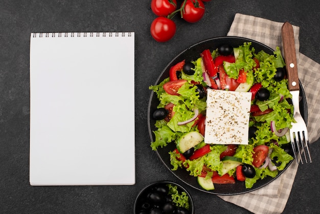 Ensalada de vista superior con queso feta y tomates con cuaderno en blanco