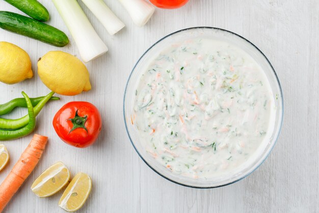 Ensalada de yogurt en un tazón con verduras y limones planos sobre una superficie de madera blanca