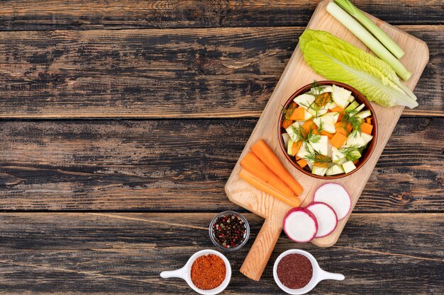 Ensalada de zanahoria en tazón de cerámica y verduras están en la vista superior de la tabla de cortar de madera con espacio de copia