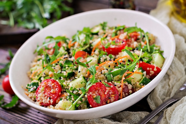 Ensaladas con quinua, rúcula, rábano, tomate y pepino en un recipiente en la mesa de madera. Comida sana, dieta, desintoxicación y concepto vegetariano.