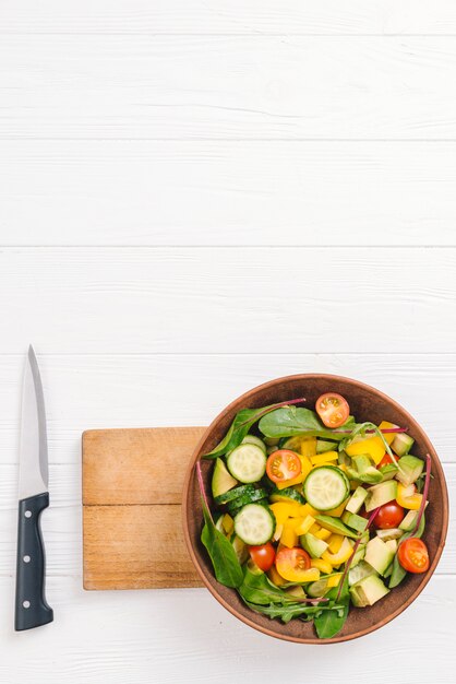 Ensaladera fresca en la tabla de cortar con un cuchillo afilado en la mesa blanca