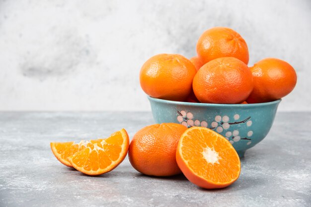 Enteras y rebanadas de jugosas frutas naranjas frescas en un recipiente colocado sobre una mesa de piedra.