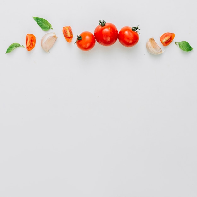 Entero y rebanada de tomates cherry; diente de ajo y albahaca sobre el fondo blanco
