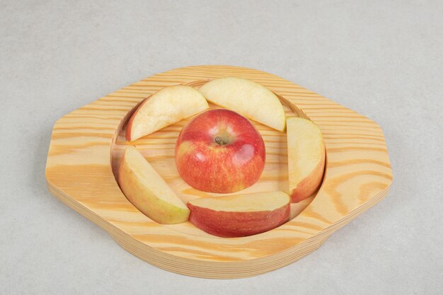 Entero y rodajas de manzana roja sobre placa de madera