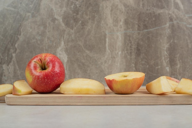 Entero y rodajas de manzana roja sobre tabla de madera