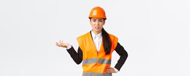 Entonces, ¿qué está pasando? Frustrada y decepcionada, la ingeniera jefa asiática se queja de que los empleados regañan a alguien que usa una chaqueta reflectante y un casco de seguridad que levanta la mano confundida.