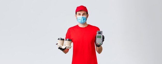 Entrega de alimentos y comestibles para llevar covid19 concepto de pedidos sin contacto Empleado amable con uniforme rojo de mensajería mascarilla y guantes que dan al cliente terminal POS con café