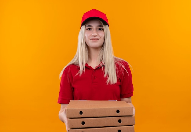 Entrega complacida joven vestida con camiseta roja y gorra con caja de pizza sobre fondo naranja aislado