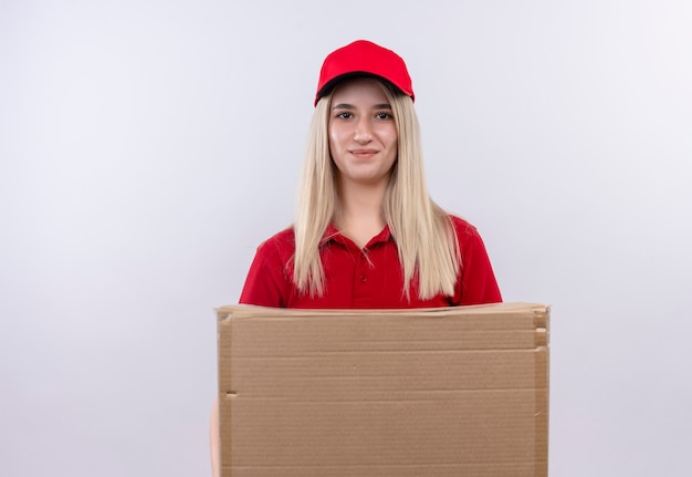 Entrega complacida joven vestida con camiseta roja y gorra con caja sobre fondo blanco aislado