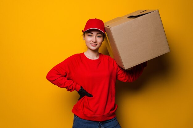 Entrega joven mujer asiática sosteniendo y llevando una caja de cartón aislada en un amarillo