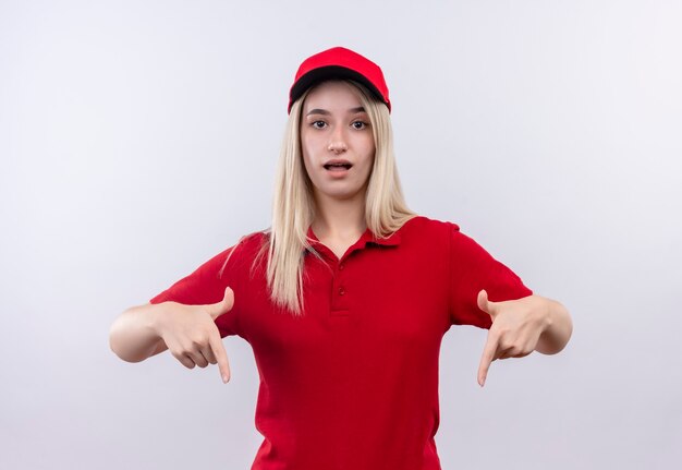 Entrega joven vistiendo camiseta roja y gorra apunta hacia abajo en la pared blanca aislada