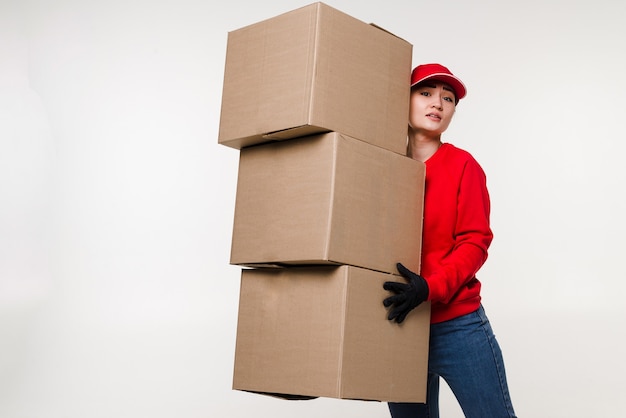 Entrega mujer asiática en uniforme rojo aislado en la pared blanca Mujer en jeans de camiseta de gorra trabajando como mensajero o distribuidor con caja de cartón