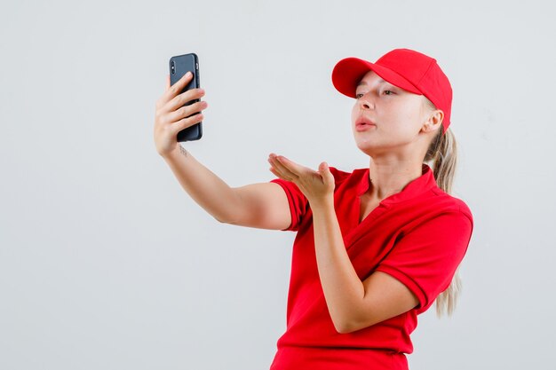 Entrega mujer enviando beso de aire en videollamada en camiseta roja y gorra