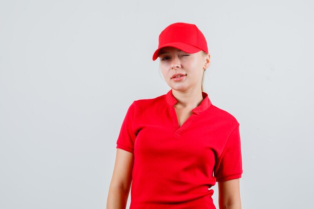 Entrega mujer guiñando el ojo en camiseta roja y gorra y mirando confiado