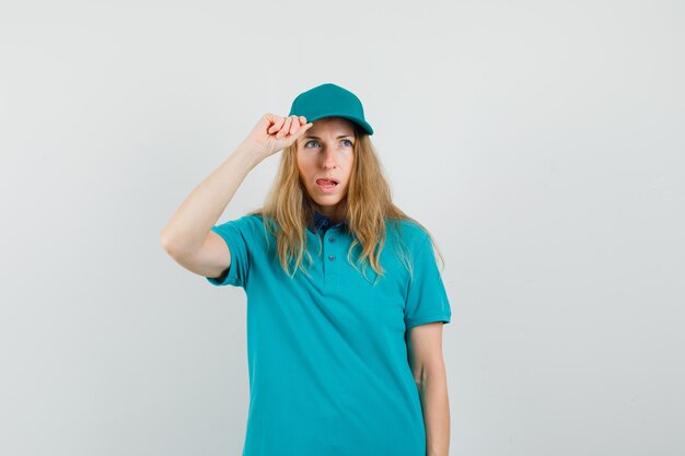 Entrega mujer sosteniendo su gorra en camiseta, gorra y mirando pensativo