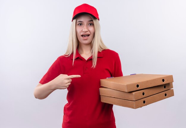 Entrega sorprendida joven vestida con camiseta roja y gorra en puntos de apoyo dental a caja de pizza en su mano sobre fondo blanco aislado