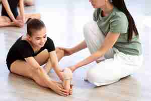 Foto gratuita entrenador de ballet femenino ayudando a la chica a estirarse durante la lección