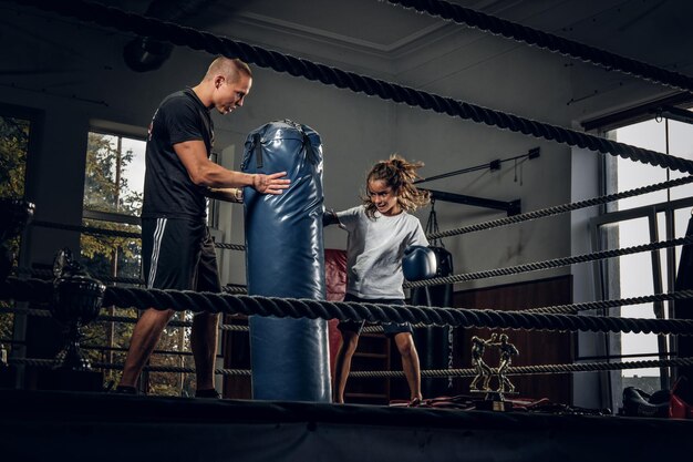 El entrenador de boxeador experimentado está entrenando a una nueva boxeadora para competencias especiales usando un saco de boxeo.