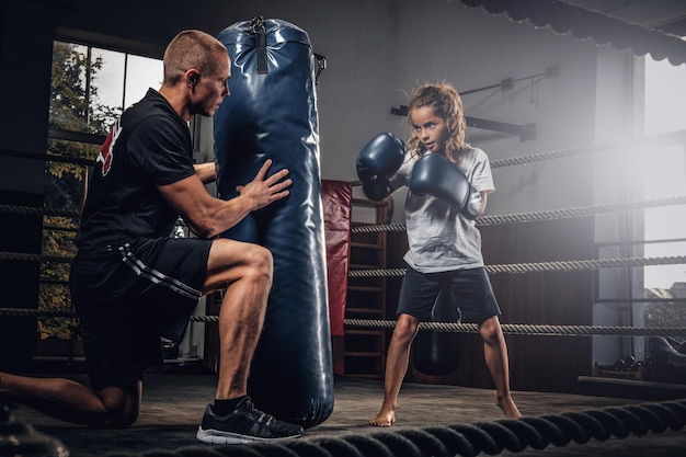 El entrenador de boxeador experimentado está entrenando a una nueva boxeadora para competencias especiales usando un saco de boxeo.