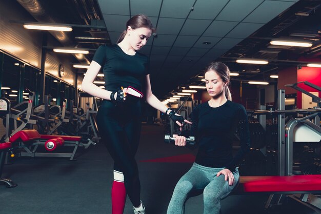 Entrenador femenino ayudar a la mujer mientras se hace ejercicio con pesas
