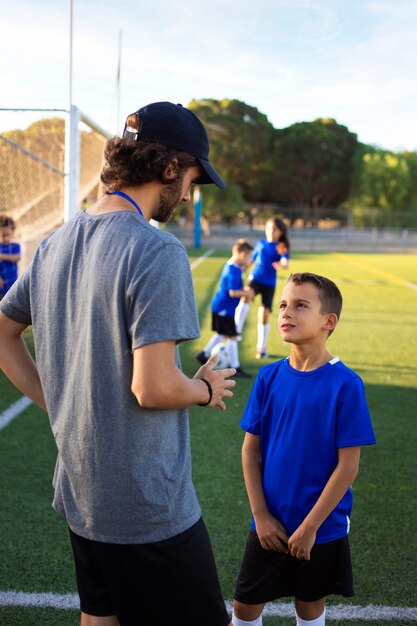 Entrenador de fútbol ayudando a niños vista lateral