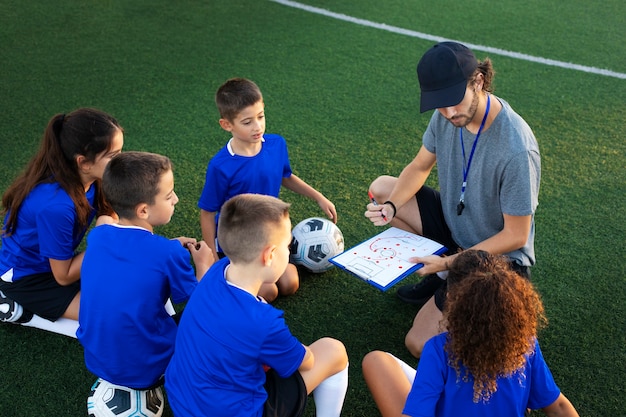 Foto gratuita entrenador de fútbol enseñando a los niños ángulo alto